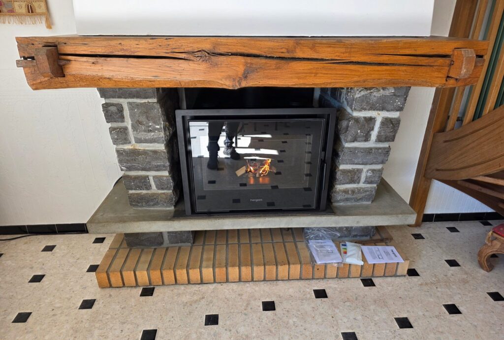 Insert à bois installé sous une poutre en bois dans une cheminée en pierre