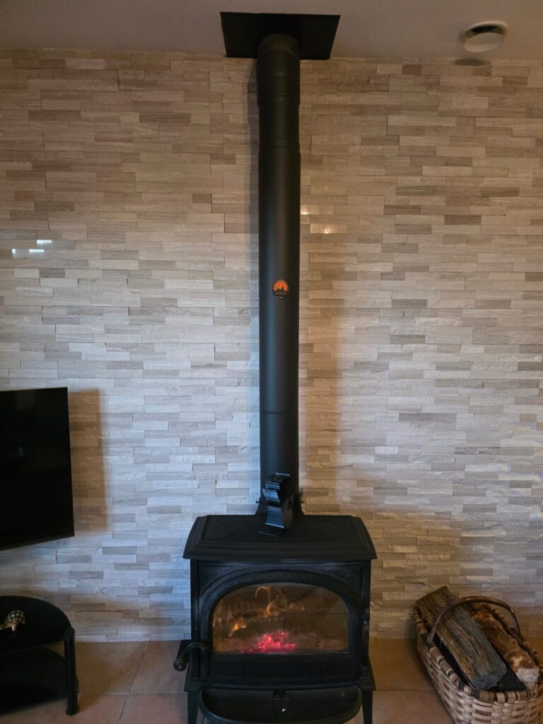 Poêle à bois noir avec conduit apparent devant un mur en plaquettes de pierre
