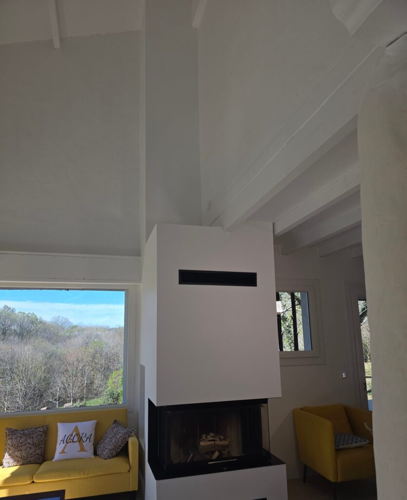 Cheminée contemporaine blanche à foyer vitré et vue sur la campagne